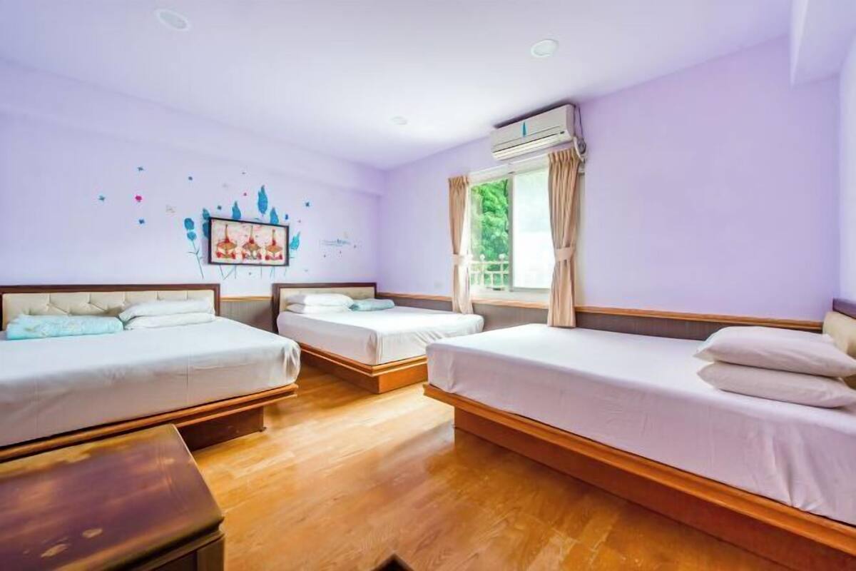Een hotelkamer met twee bedden, een houten vloer, een raam met gordijnen en een decoratie aan de muur.