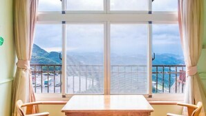Ein Zimmer mit Tisch und zwei Stühlen, ein großes Fenster mit Bergblick und einem Balkon.