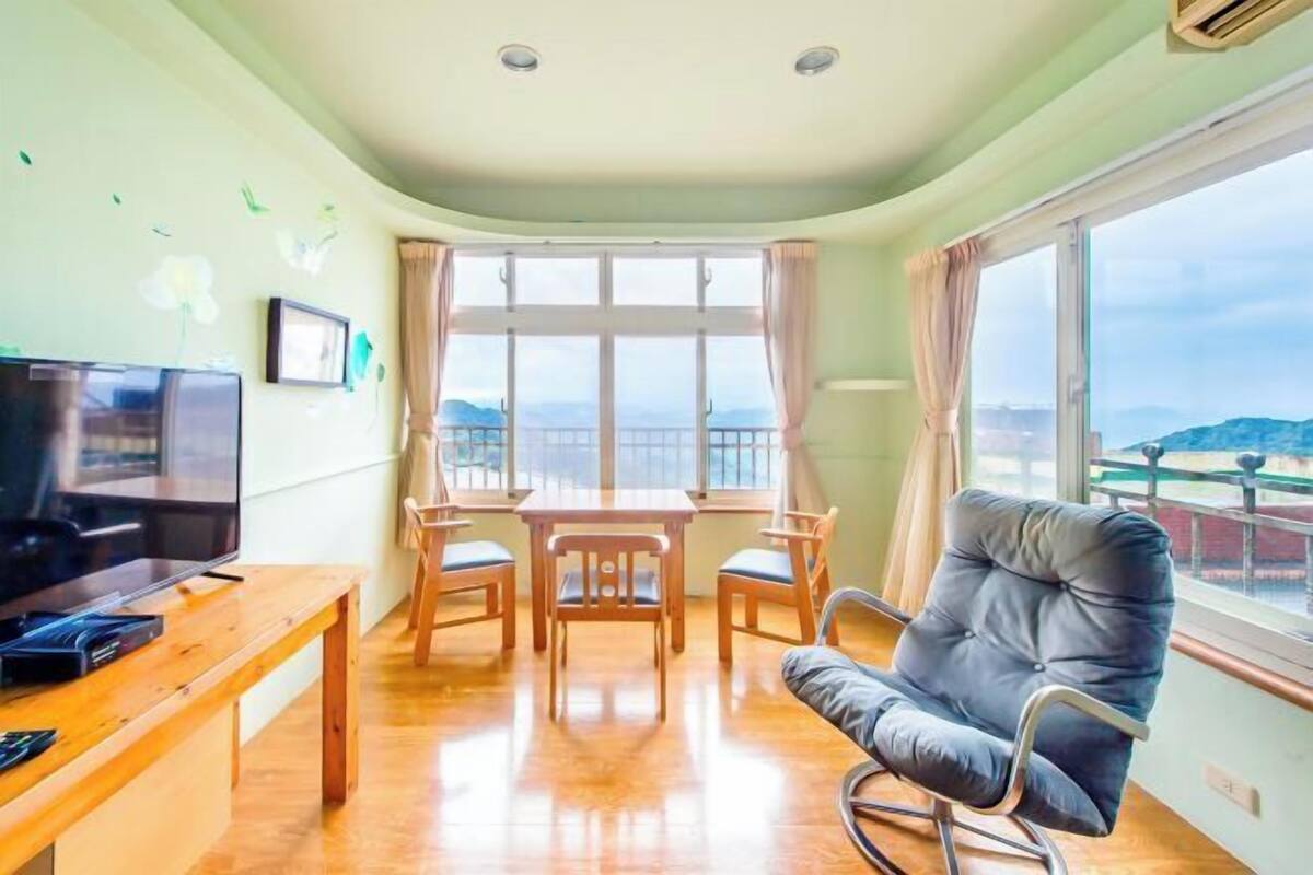 Een kamer met een televisie, houten meubels, een balkon en een uitzicht.
