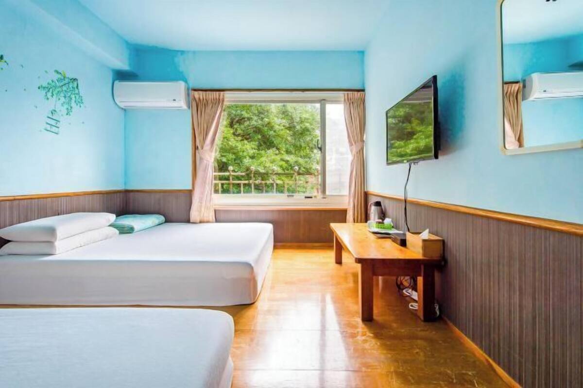 Een hotelkamer met twee bedden, een houten tafel, een televisie en een raam met gordijnen.