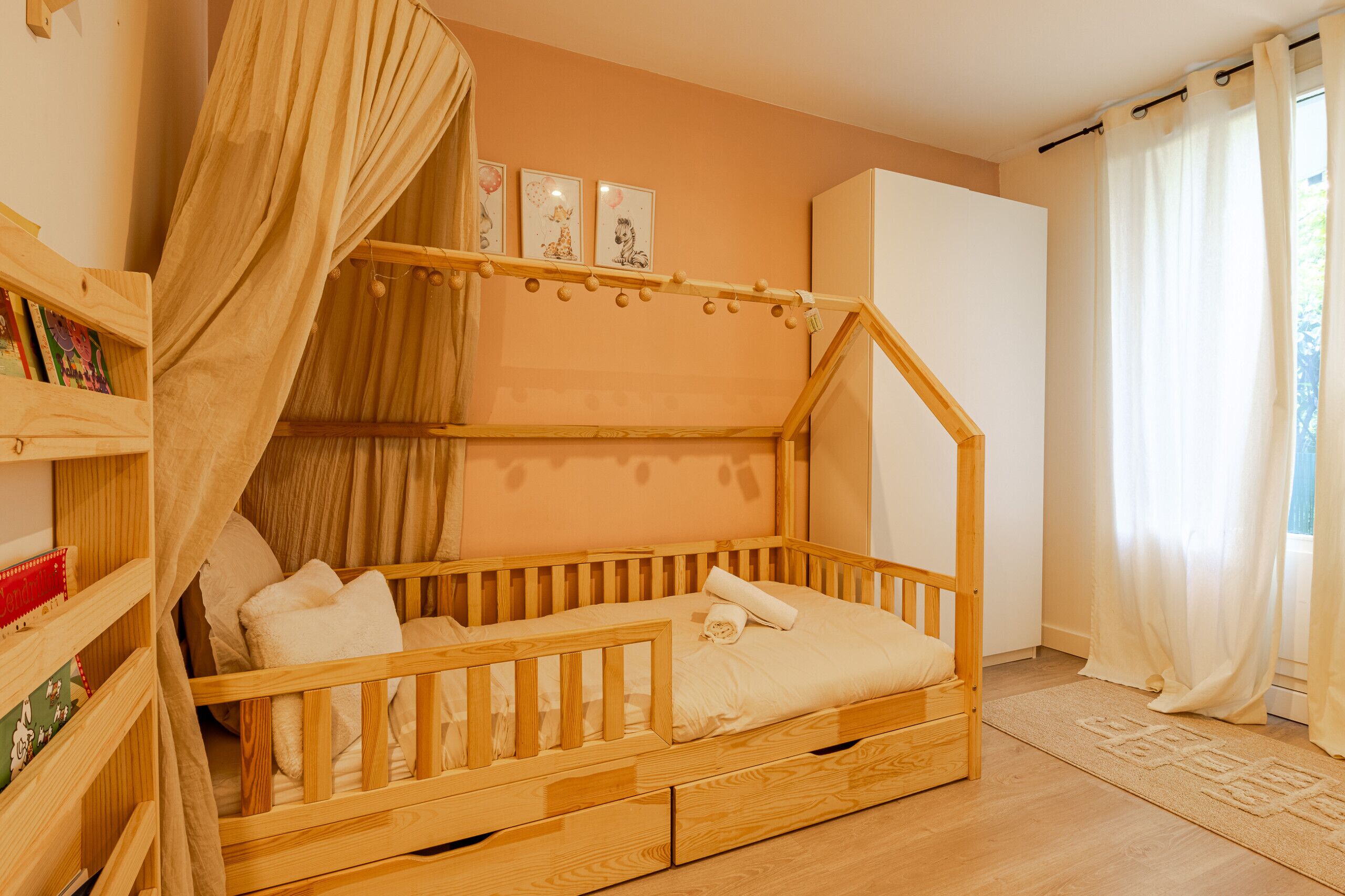 Una cama litera de madera con dosel, una estantería y un pequeño escritorio.