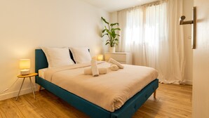 A neatly made bed with a blue headboard, a bedside lamp, and a potted plant.