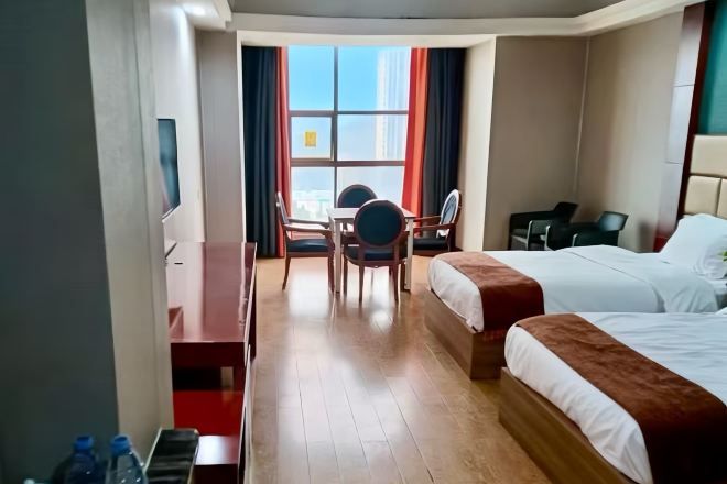A hotel room with two beds, a desk, a chair, and a window with curtains.