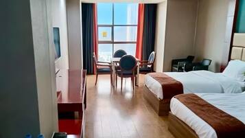 A hotel room with two beds, a desk, a chair, and a window with curtains.