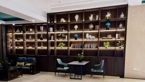 A modern interior with a dark wood shelving unit displaying various decorative items and books. There is a seating area with a sofa and chairs, and a small table with a plant. - Pai Hotel (Chenzhou Yizhang County Yiren Plaza Branch) (Yizhang)
