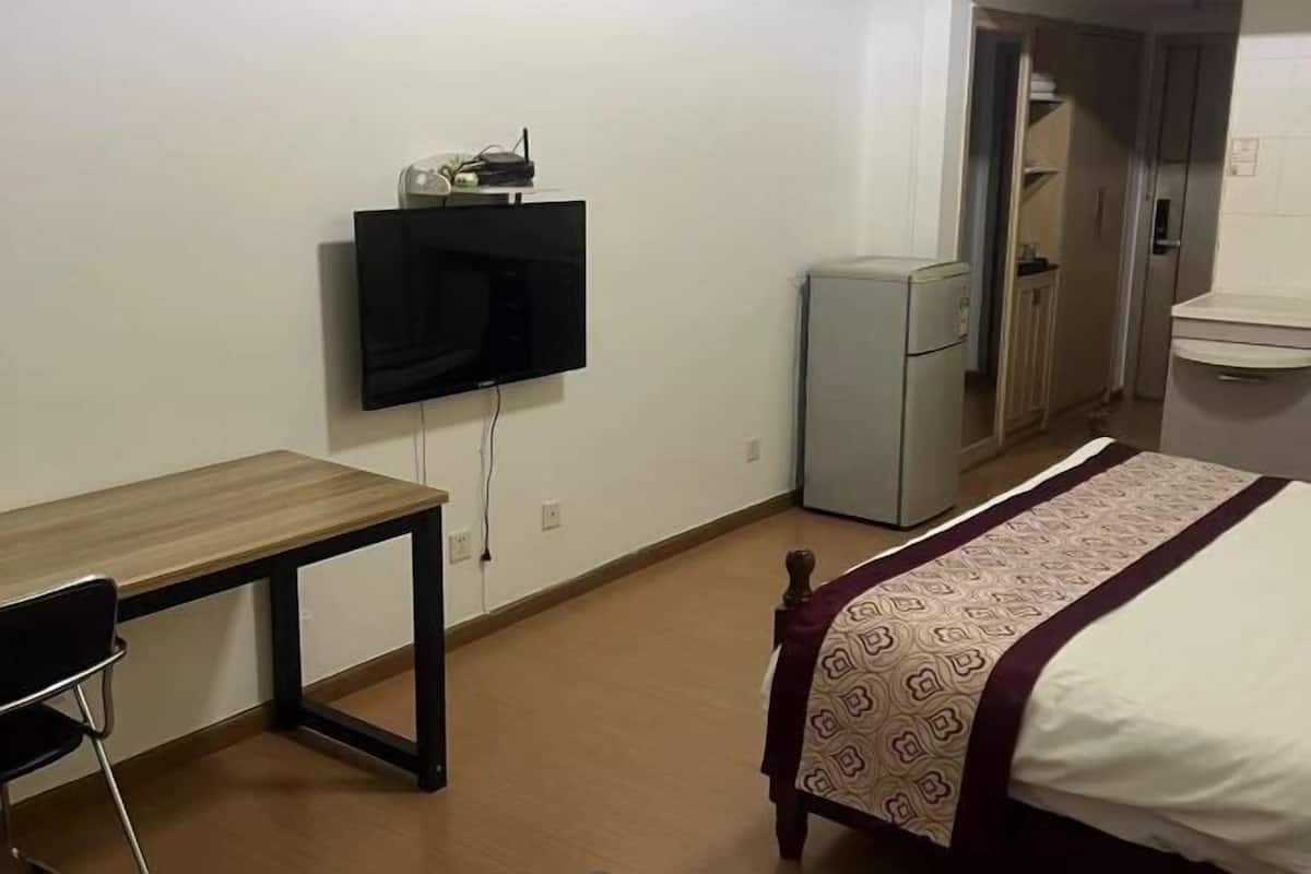 Een slaapkamer met een bed, een bureau, een televisie, een koelkast en een badkamer.