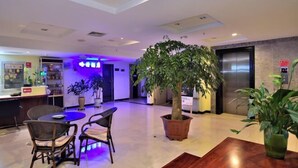 En hotellobby med receptionsdisk, siddeområde og en stor stueplante.