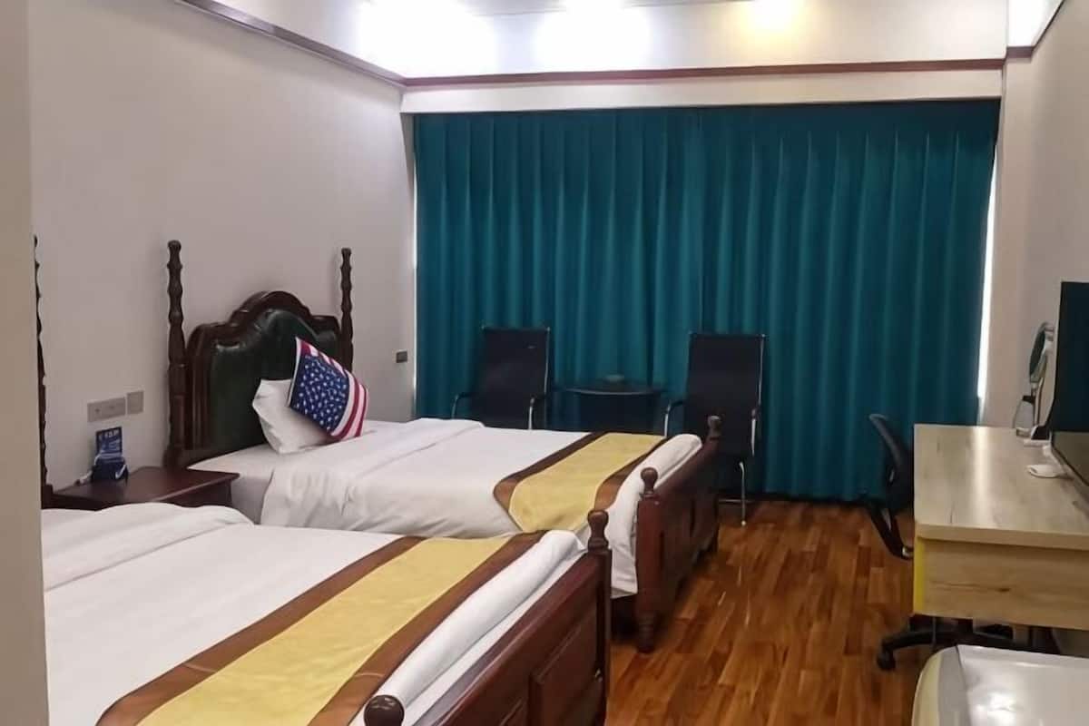 Hotelkamer met twee bedden, een bureau, een stoel, een televisie en een raam met gordijnen.