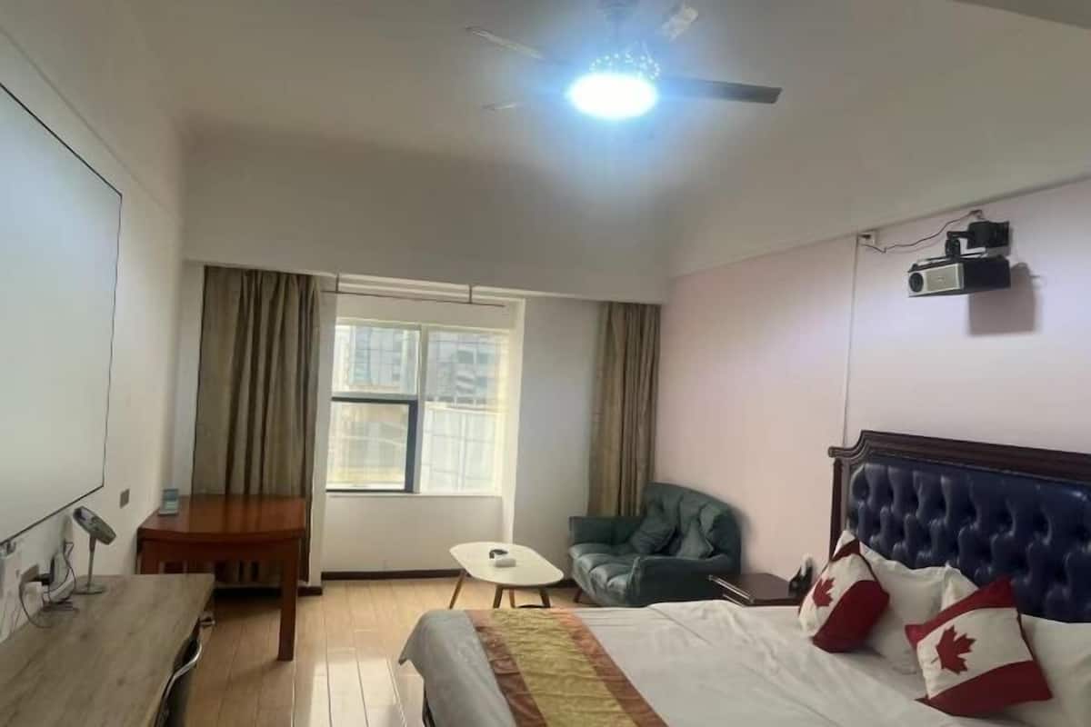 Hotelkamer met een bed, bureau, stoel, klein tafeltje, plafondventilator en raam met gordijnen.