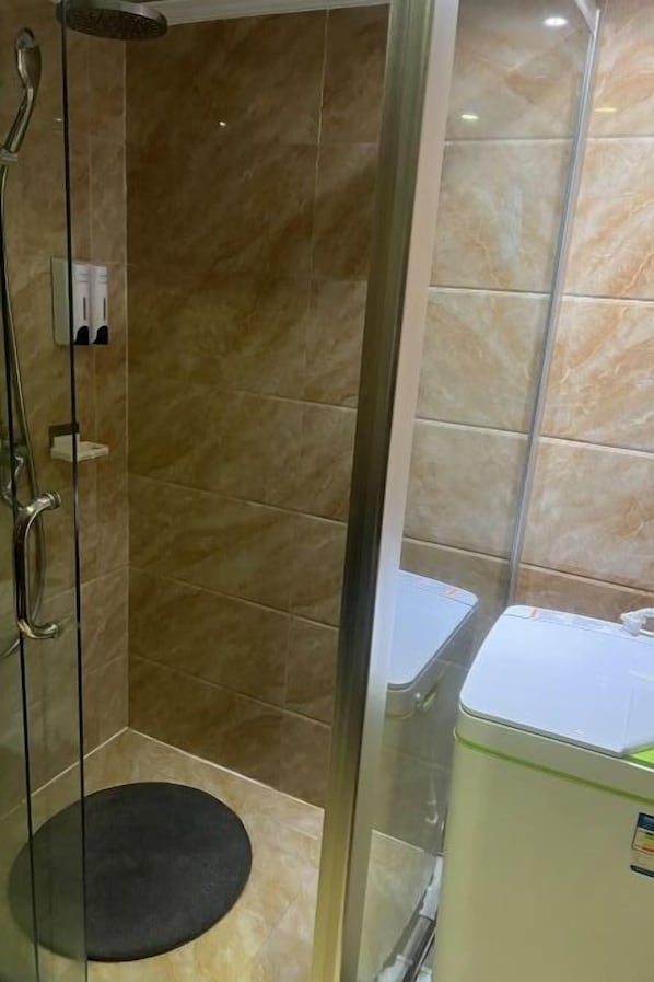 Een douche met een glazen deur, een handdouche en een zwart rond tapijt.