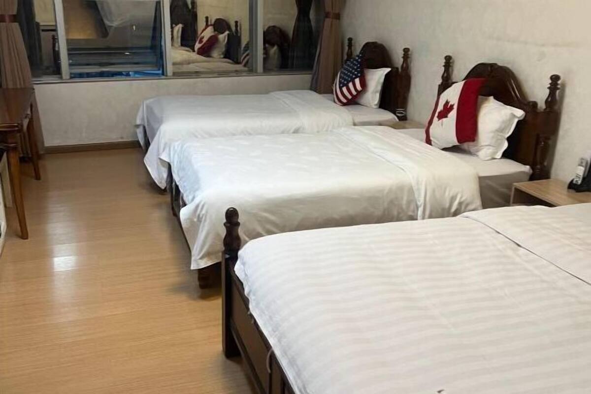 Een hotelkamer met twee bedden, een houten vloer, een raam met uitzicht en een spiegel.