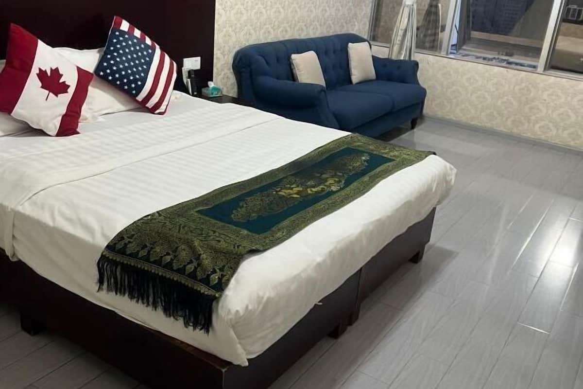 Een bed met een wit laken en een decoratieve plaid, een blauwe bank met kussens, en een raam met uitzicht.