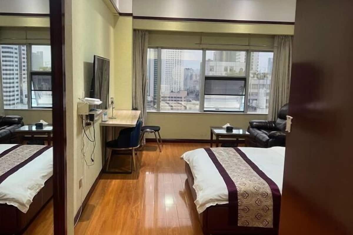Een hotelkamer met twee bedden, een bureau, een stoel, een televisie en een raam met uitzicht op de stad.
