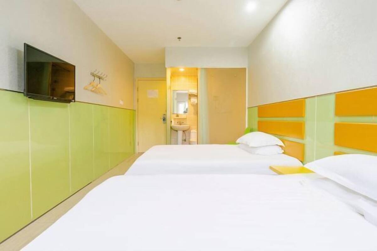 A hotel room with two beds, a television mounted on the wall, and a bathroom visible through an open door.