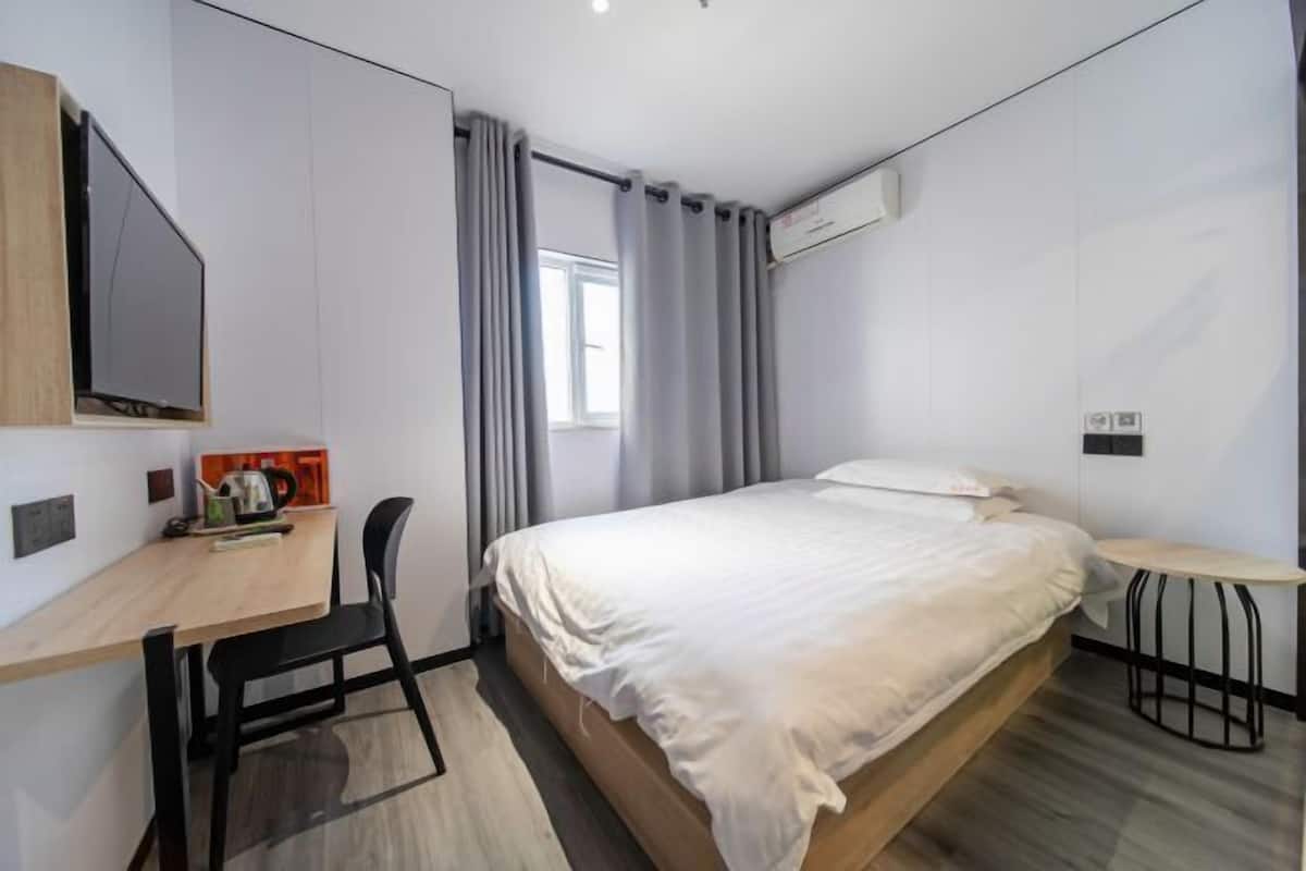 A modern hotel room with a bed, a desk with a chair, a small table, and a TV.