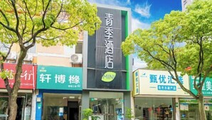 A hotel with a prominent sign in the center, surrounded by various storefronts. - Changee Hotel MINI (Shanghai Jinshan City Beach) (Shanghai)