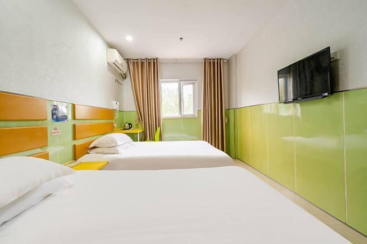 A hotel room with two beds, a TV on the wall, and a window with curtains.