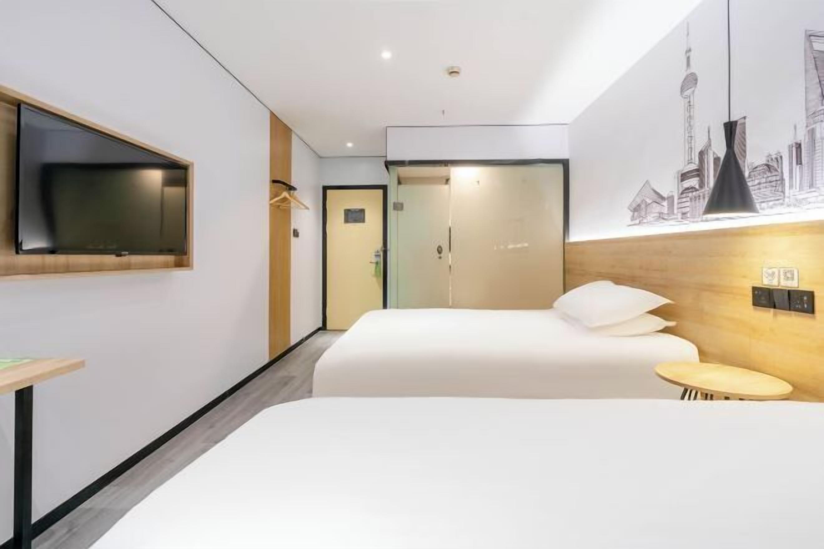 Ein Hotelzimmer mit Bett, Wandfernseher, kleinem Tisch und Wandlampe.