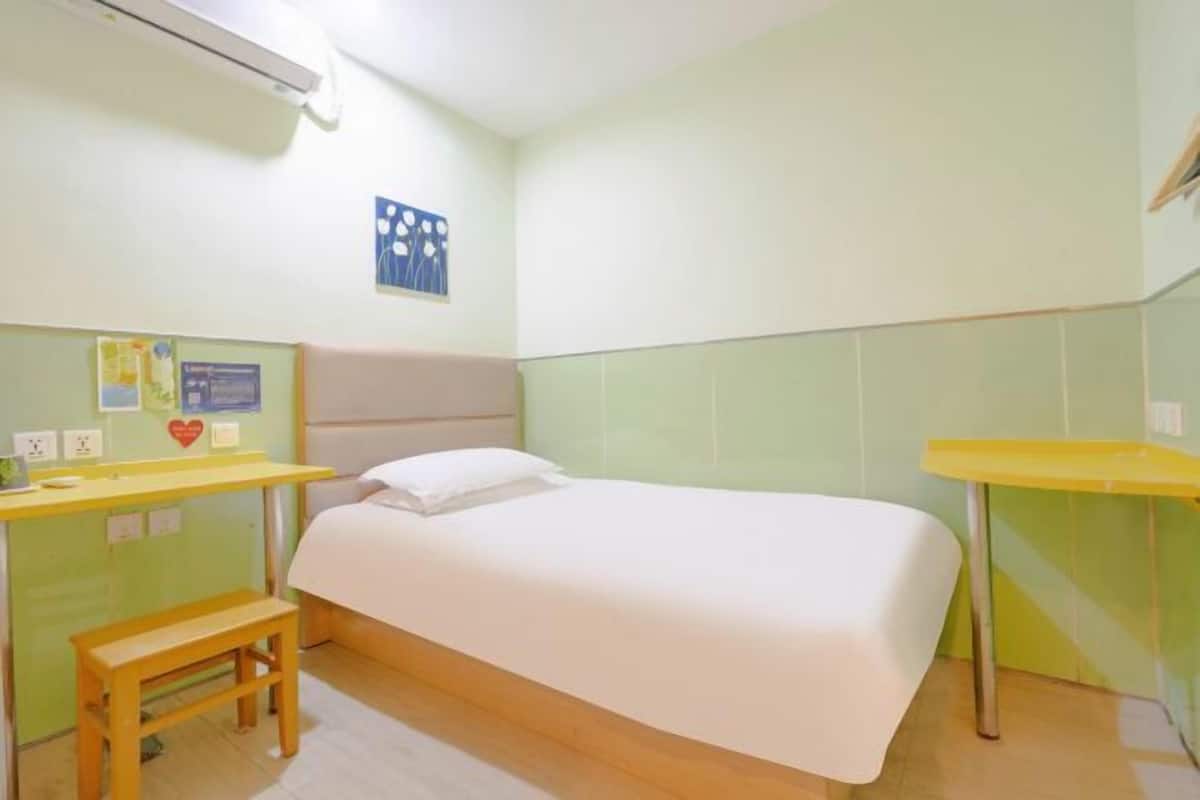A single-bed room with a wooden bench, a small table, and a wall-mounted shelf.