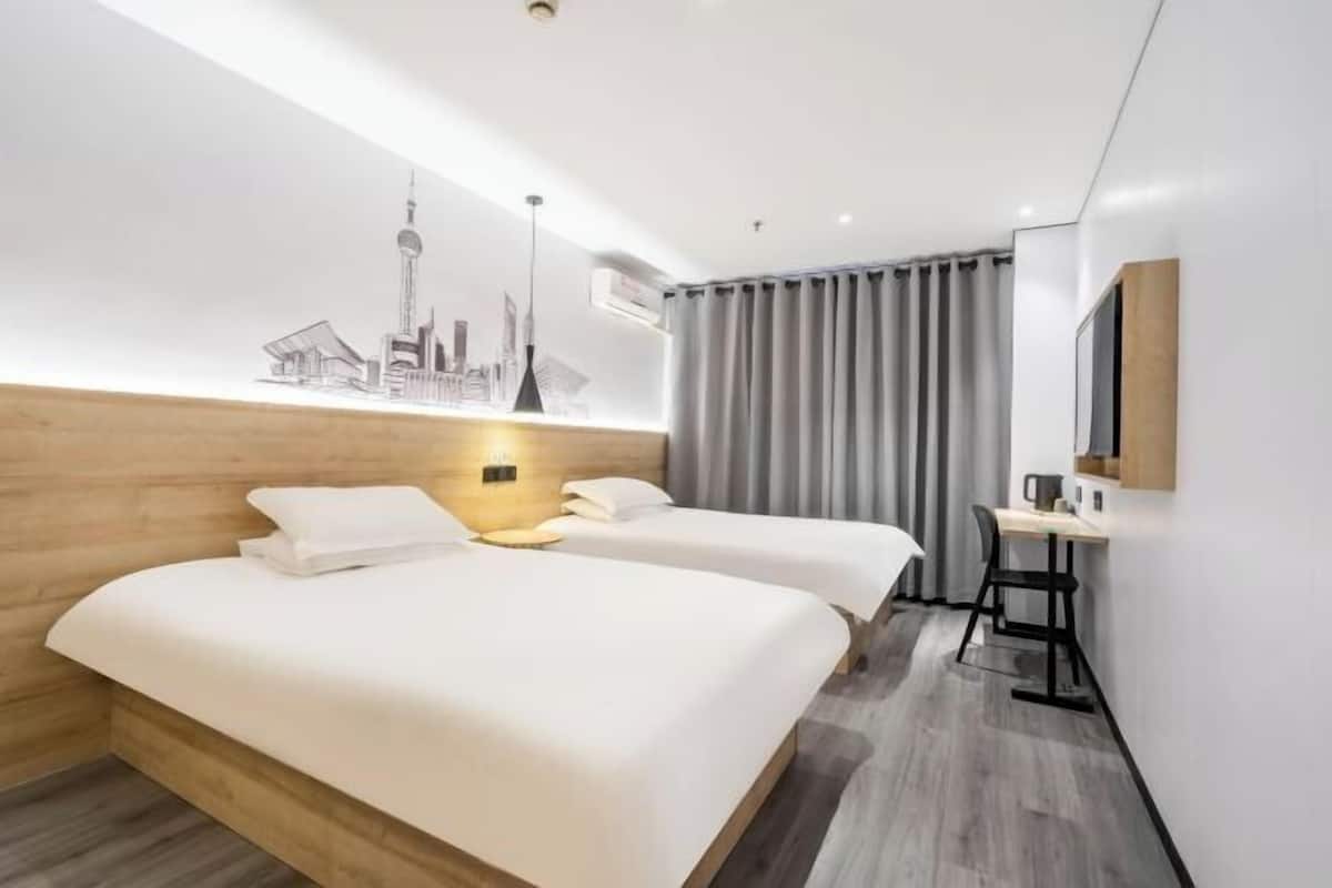 A hotel room with two beds, a desk, a mirror, and a cityscape artwork on the wall.