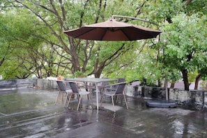 Un espace extérieur aménagé pour les repas, avec une table, des chaises, un parasol et un élément décoratif aquatique.