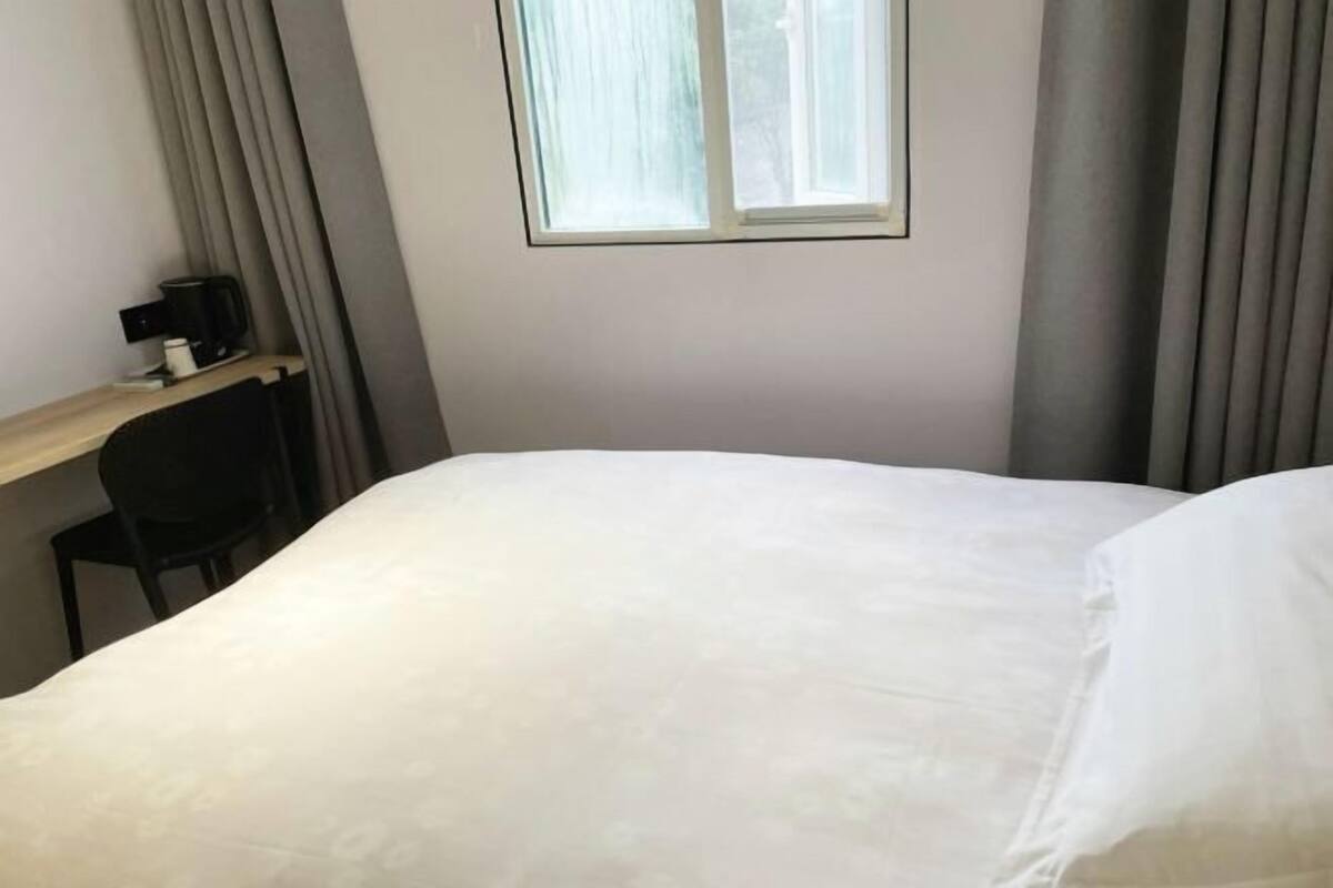 A hotel room with a bed, a desk with a chair, a window, and curtains.