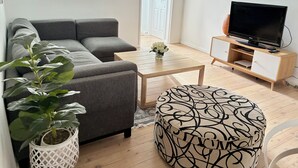A living room with a sofa, ottoman, coffee table, TV stand, and a potted plant. - Beachside townhouse at Mona Vale beach, spacious and modern , footsteps to beach (Mona Vale)