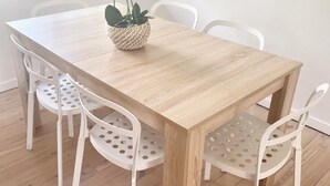A wooden dining table with a woven pot of white flowers, surrounded by white chairs with perforated backs. - Beachside townhouse at Mona Vale beach, spacious and modern , footsteps to beach (Mona Vale)