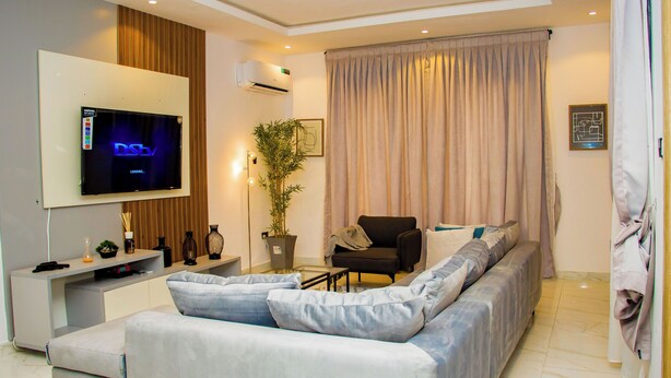A modern living room with a large flat-screen TV, a sofa, a chair, and a potted plant.
