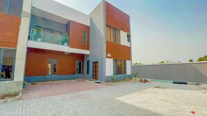 A modern two-story building with a flat roof, large windows, and a visible balcony.