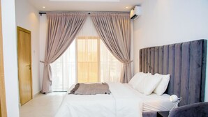 A modern bedroom with a large bed, a headboard, and a window with curtains.