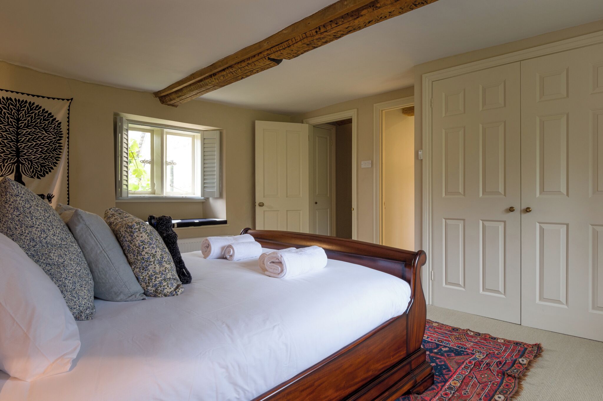 Un dormitorio con cama de madera, ropa de cama blanca y alfombra estampada.