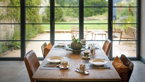 A dining area with a wooden table set for four, surrounded by chairs with brown cushions. - The Mill House Beautiful 4BD Family Home (Stroud)