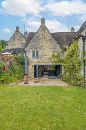A stone house with a garden patio, a dining area, and a visible kitchen. - The Mill House Beautiful 4BD Family Home (Stroud)