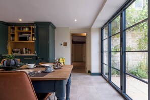 A dining area with a wooden table, chairs, and a kitchen with open cabinets. - The Mill House Beautiful 4BD Family Home (Stroud)