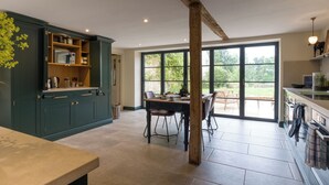 A spacious kitchen with a large dining table, built-in cabinetry, and a view through large windows to an outdoor area. - The Mill House Beautiful 4BD Family Home (Stroud)