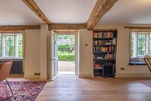 A spacious room with wooden beams, a bookshelf, and a view of a garden through an open door. - The Mill House Beautiful 4BD Family Home (Stroud)