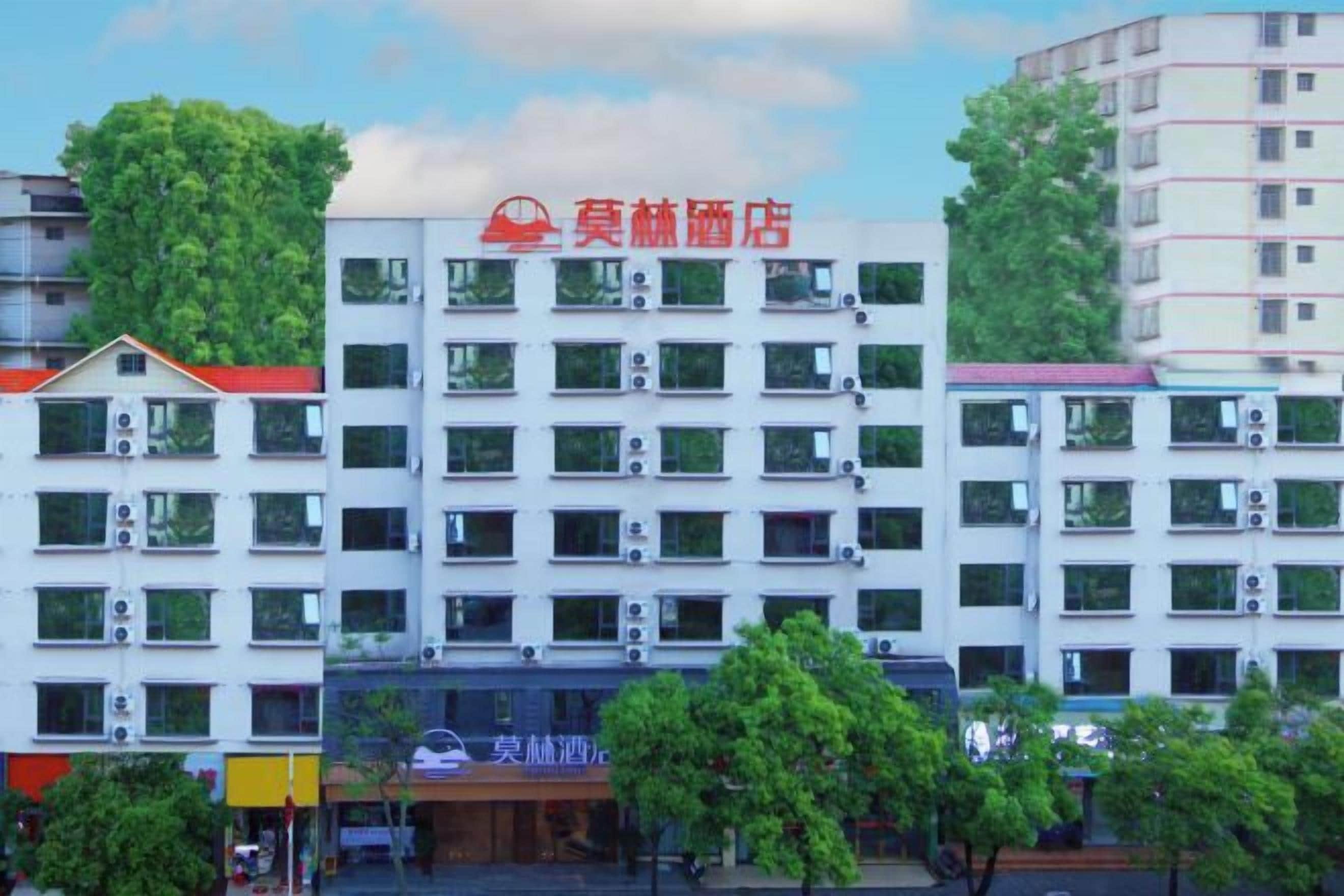 A multi-story hotel with a prominent red sign, air conditioning units, and a clear view of the surrounding buildings.