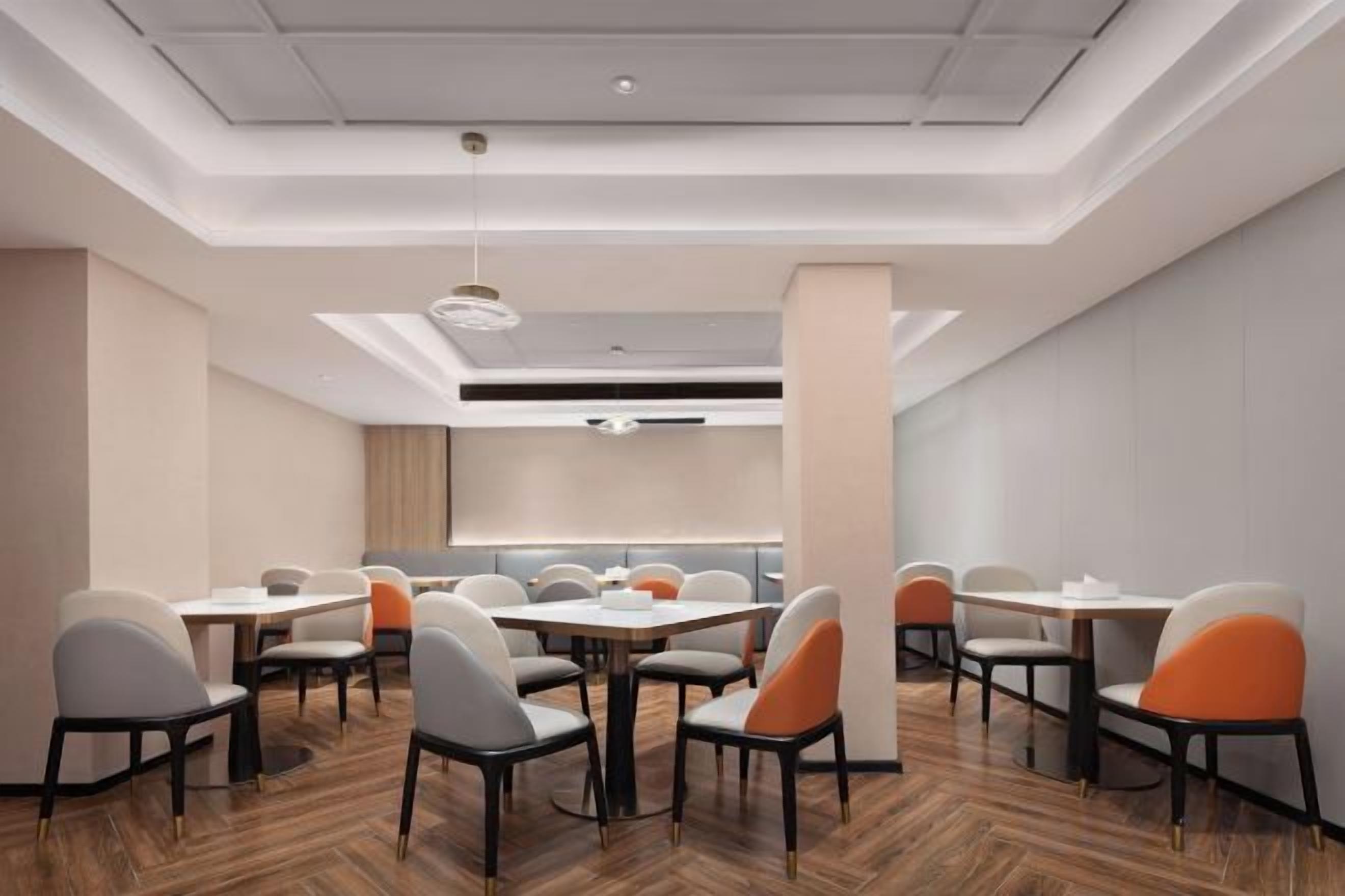 A modern conference room with tables and chairs, a wooden floor, and a ceiling with recessed lighting.