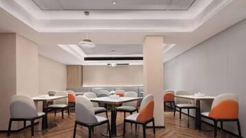 A modern conference room with tables and chairs, a wooden floor, and a ceiling with recessed lighting.