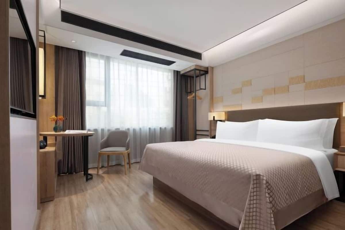 A hotel room with a large bed, a desk, a chair, and a window with curtains.