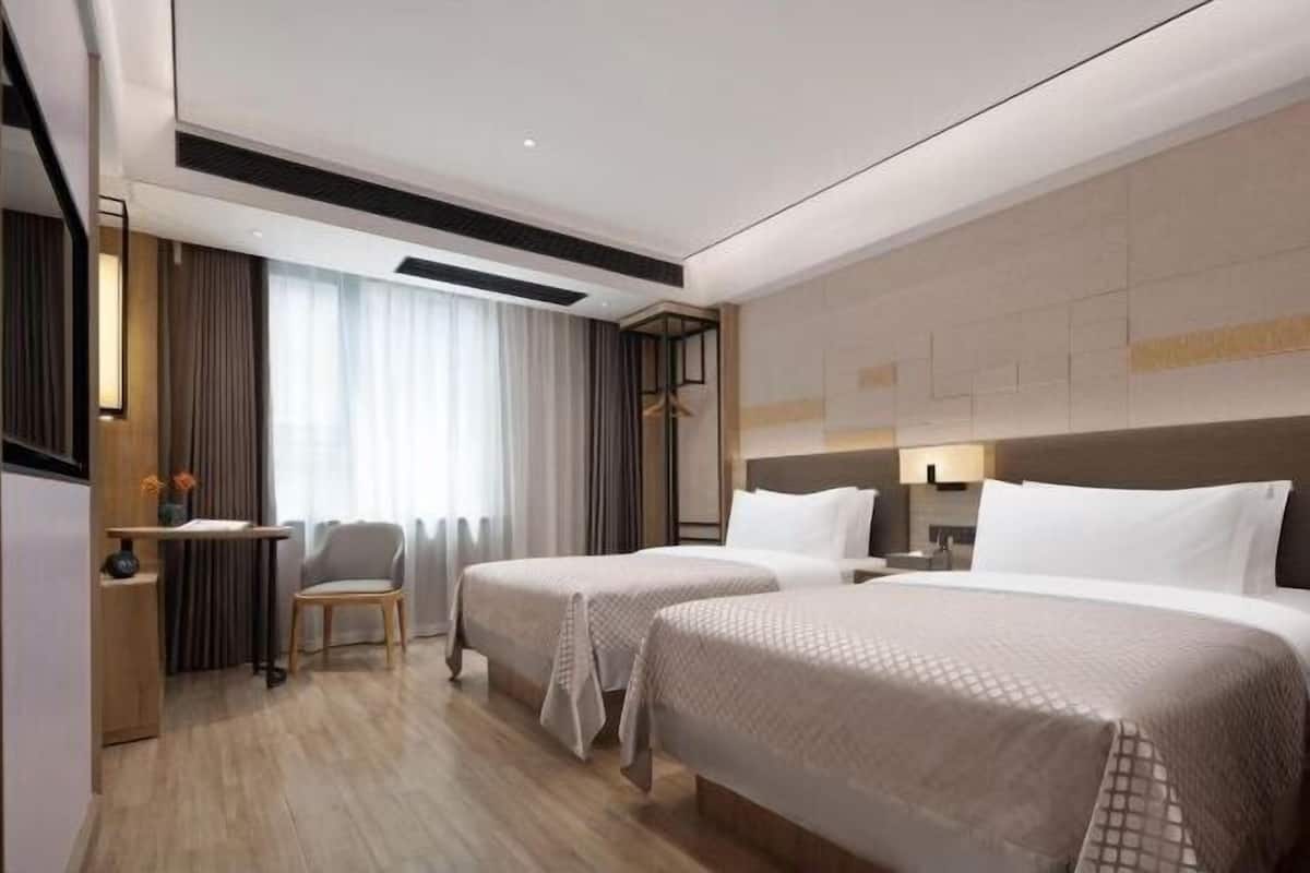 A hotel room with two beds, a desk, a chair, and a large window with curtains.