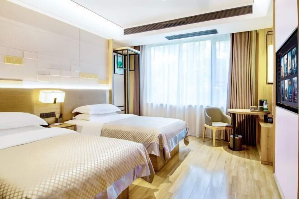 A hotel room with two beds, a desk, a chair, and a large window with curtains.