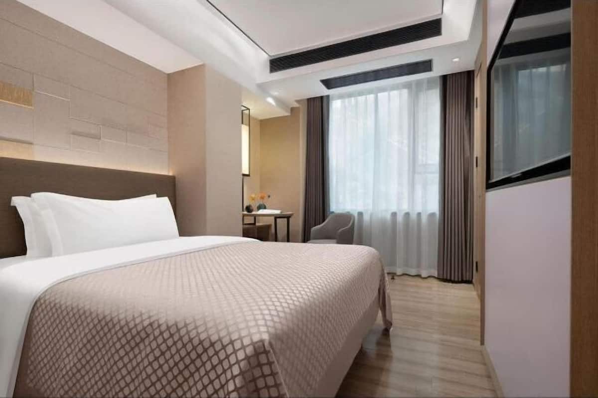 A hotel room with a large bed, a desk, a chair, and a window with curtains.