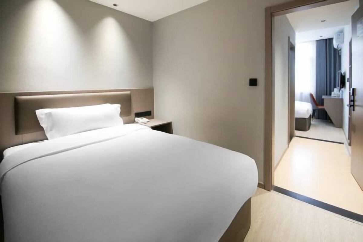 A modern hotel room with a large bed, a nightstand, and a view of the hallway.