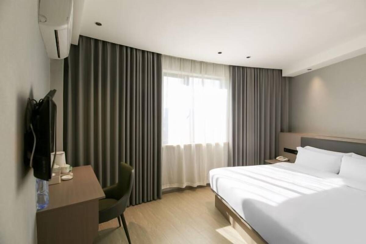 A hotel room with a bed, a desk, a chair, a nightstand, and a window with curtains.