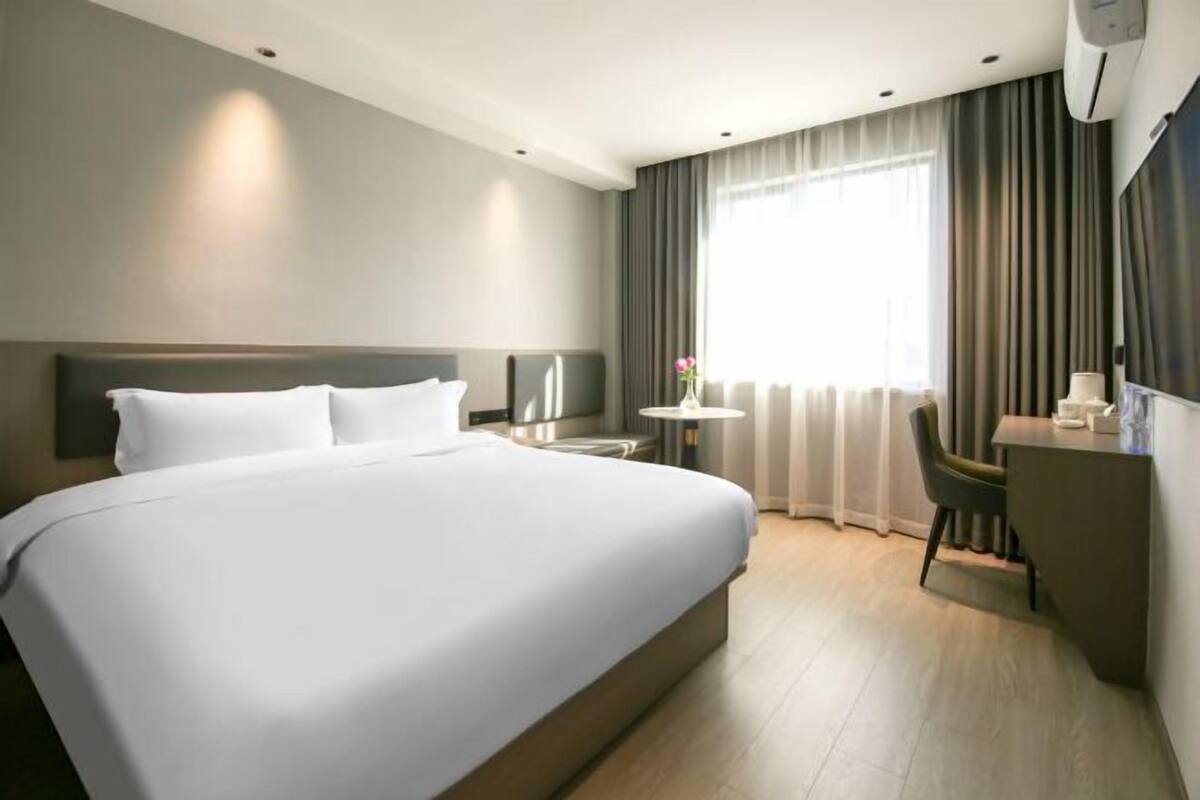 A hotel room with a large bed, a desk, a chair, a small table, and a window with curtains.