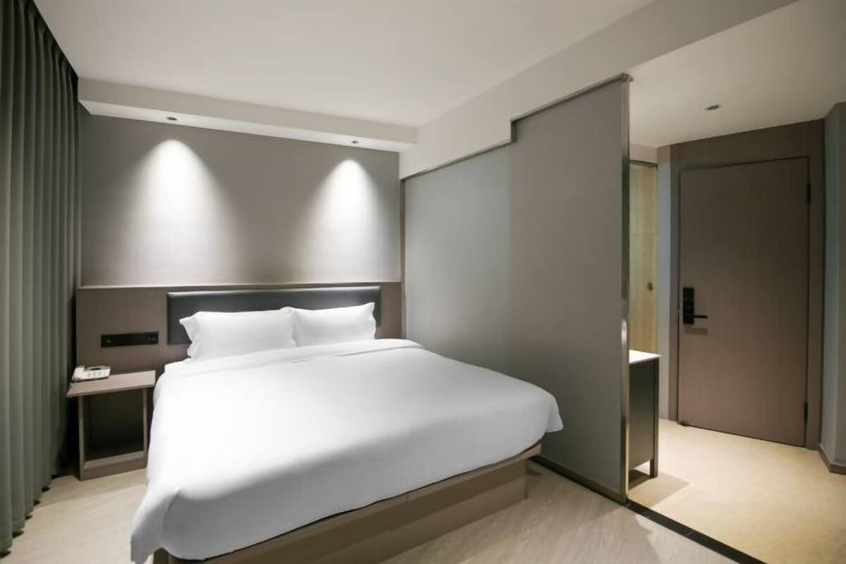 A modern hotel room with a large bed, bedside tables, and a wardrobe.