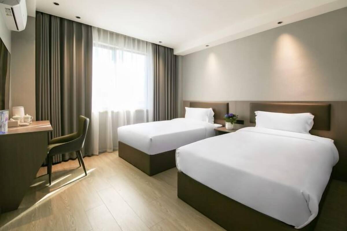 A hotel room with two beds, a desk, a chair, and a window with curtains.