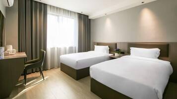 Une chambre d’hôtel avec deux lits, un bureau, une chaise et une fenêtre avec des rideaux.